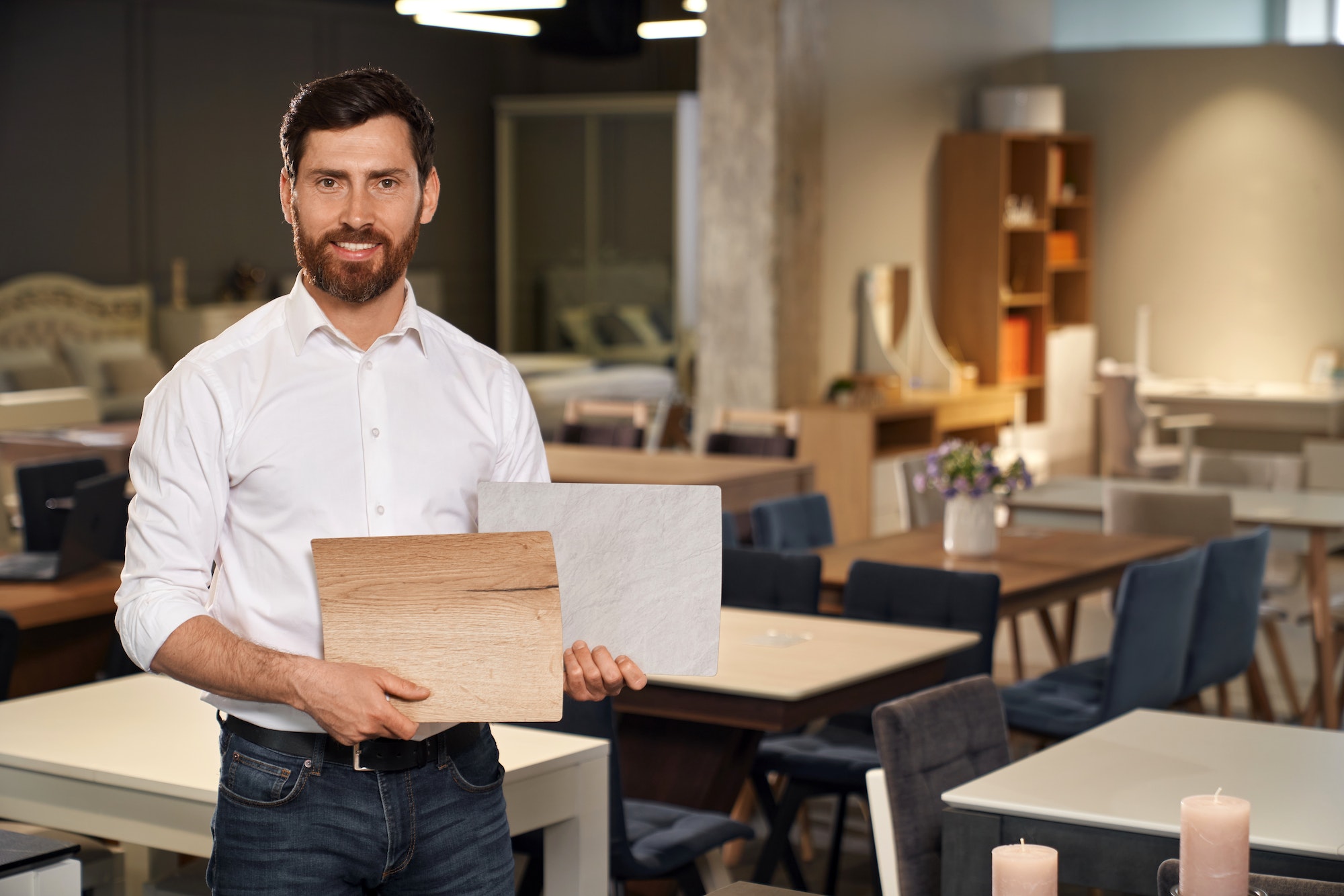 Smiling male interior designer presenting wooden laminated samples for selection in furniture store.